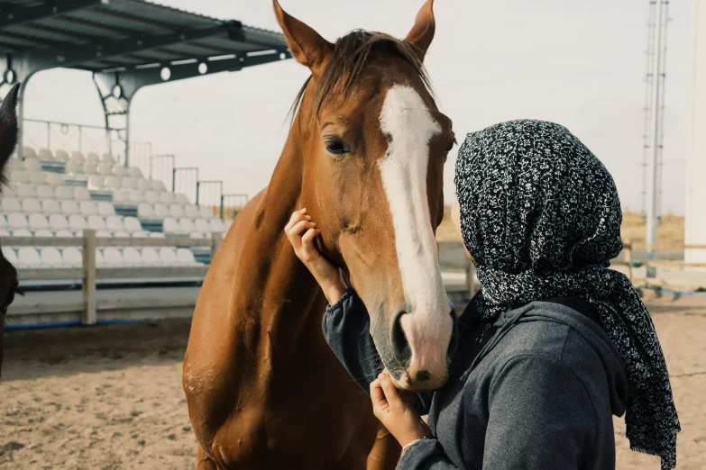 the woman holds her head next to a brown horse