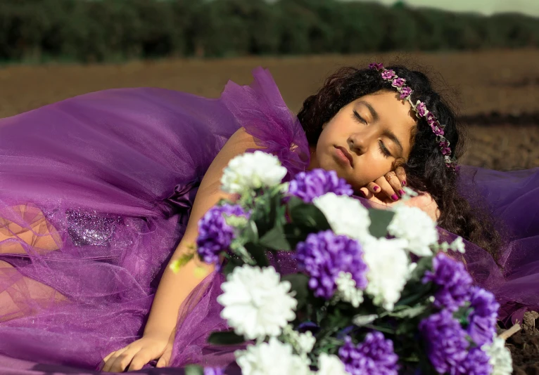 a little girl laying in the ground with purple tutu and her flowers