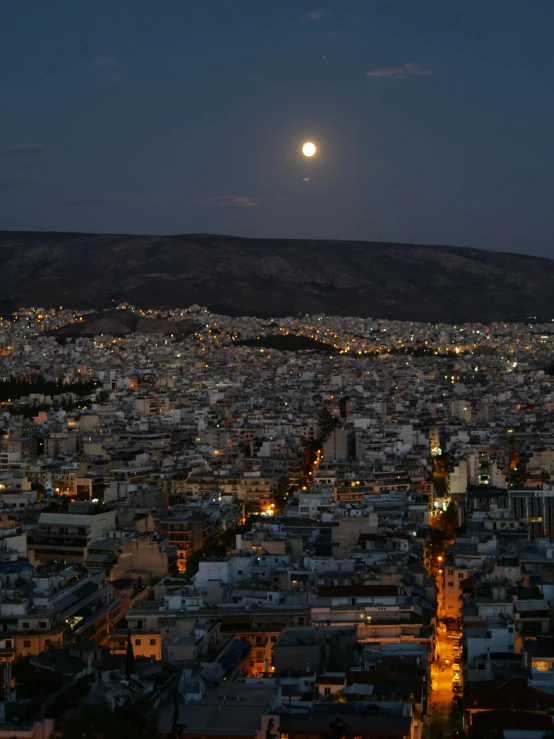 the night sky with a full moon, a distant view of the city