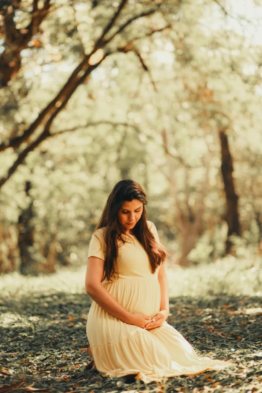 a pregnant woman in a dress sitting on the ground