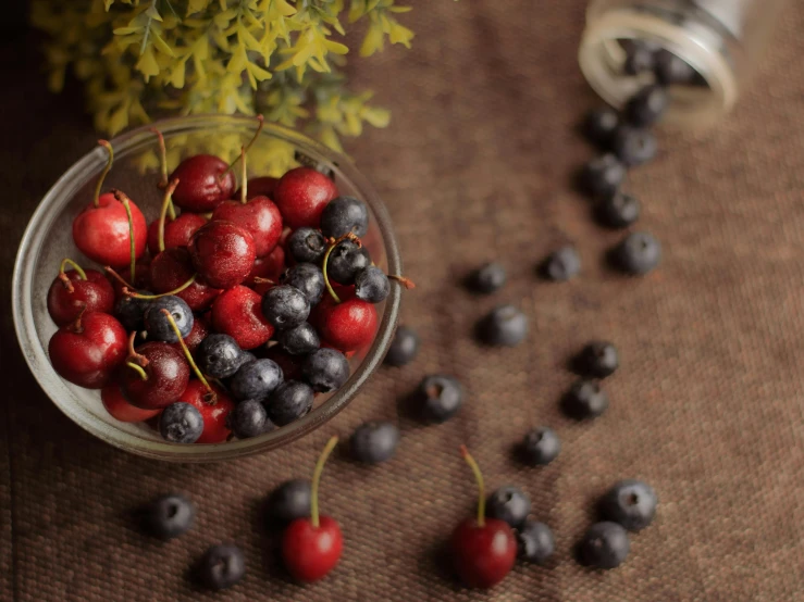 black and red cherries are in a bowl next to some yellow flowers