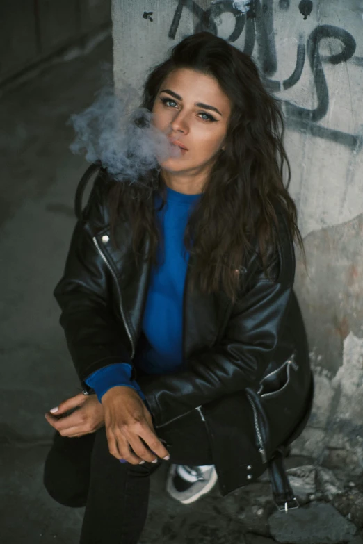 a woman smoking a cigarette in front of a graffiti - covered wall