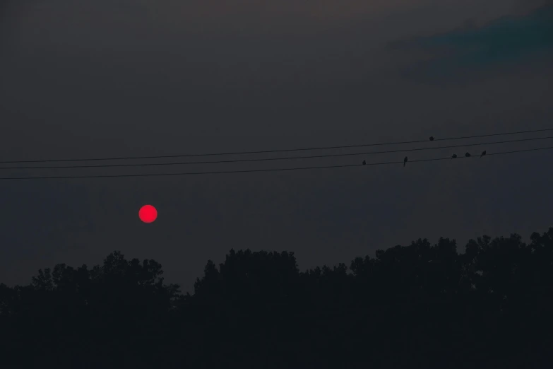 red ball of  against black sky in front of power lines