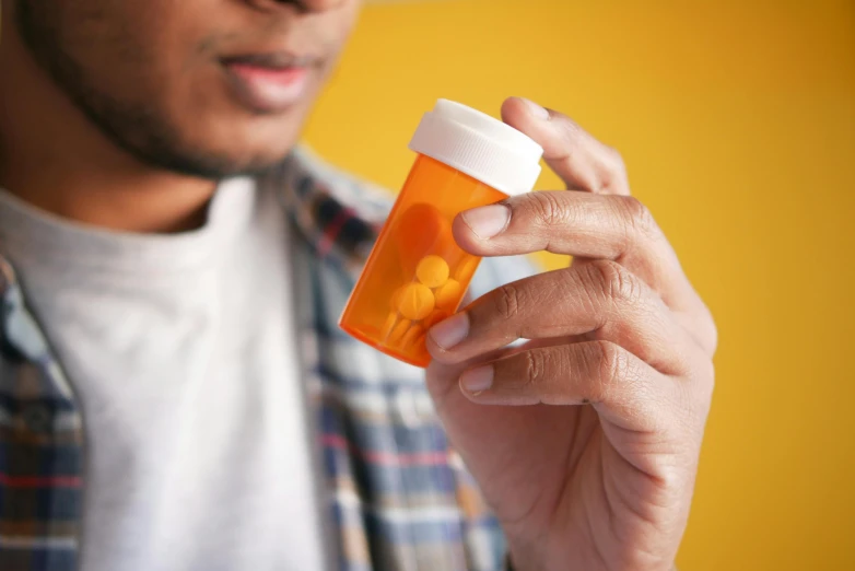 a man holding a bottle of orange pills in one hand