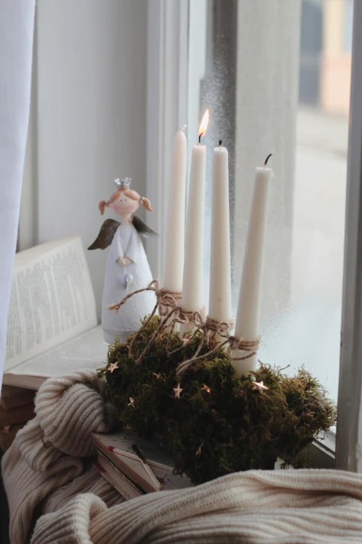 four candles, twigs and fairy doll on a window sill