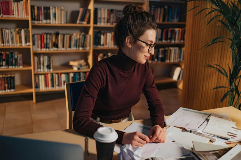 a woman in glasses is sitting at a desk and looking down at some papers