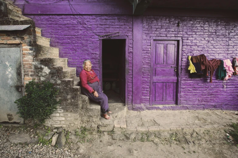 a woman sitting outside a purple building with clothes on the clothes line