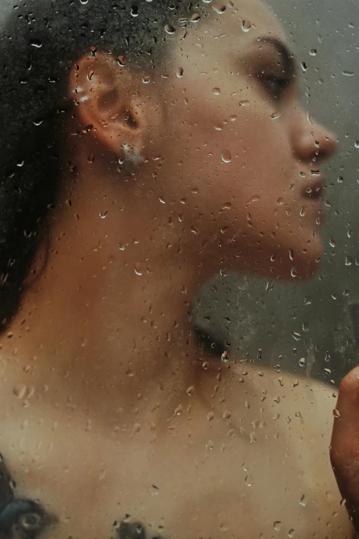 a young woman is seen through the rain on a glass