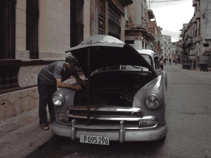 man repairing car's front grill and hood, in urban area
