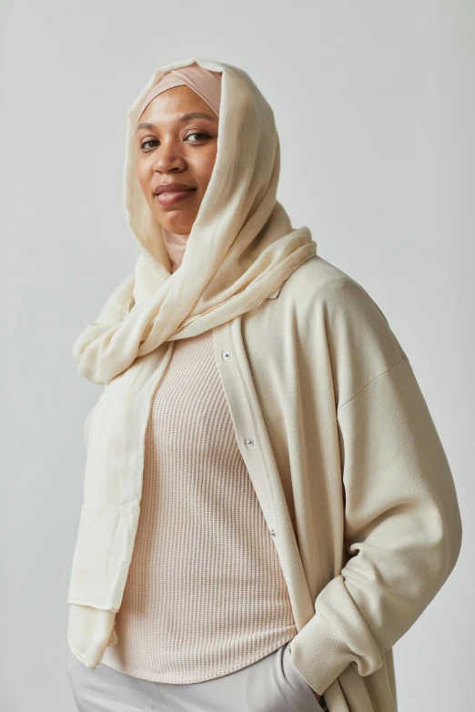 a woman is standing wearing a cream outfit and a head scarf