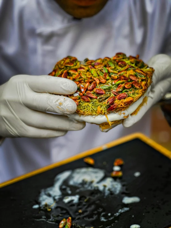 a man wearing gloves holding a sandwich with pistachio seeds