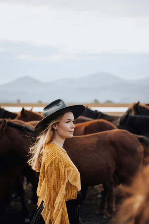 woman wearing a hat standing between a herd of horses