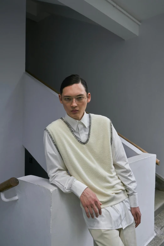 a man in a sweater and dress pants poses in a stairwell