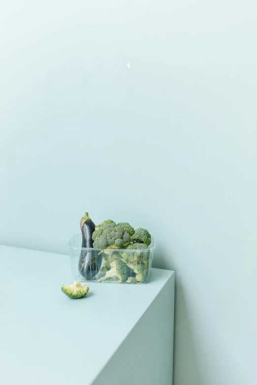 a plastic cup of broccoli sitting on top of a white shelf