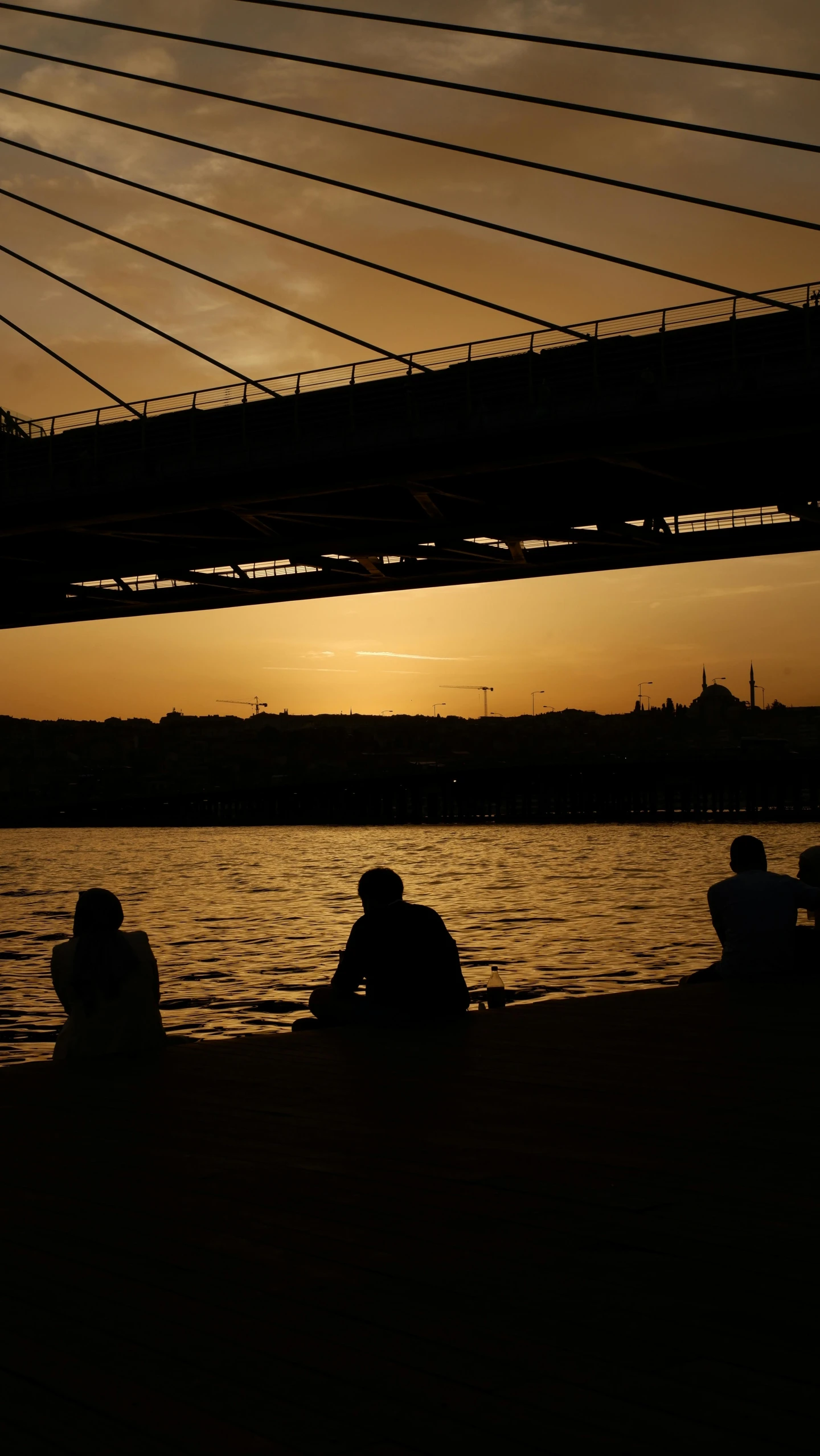 three people are sitting under an overpass looking out at the water