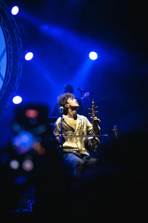 the musician sits in front of blue and white lights