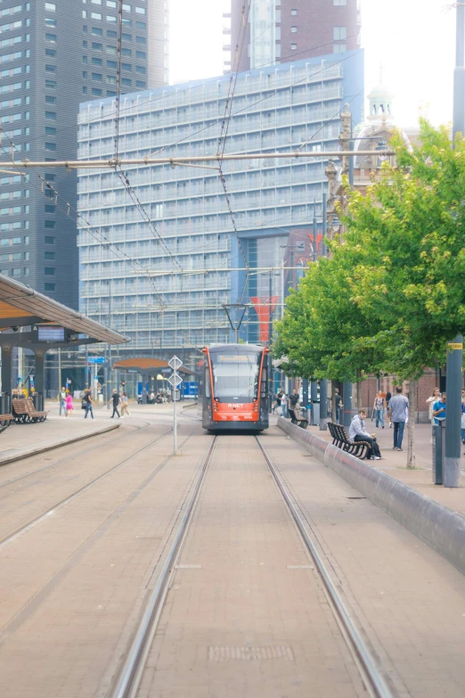 a red and orange train traveling down tracks near tall buildings