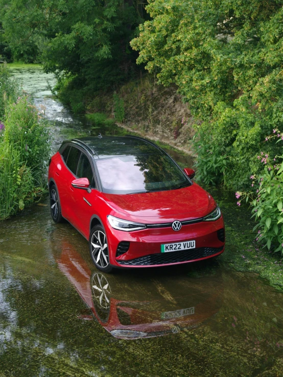 a red volkswagen e - tronic is driving through the water in front of trees