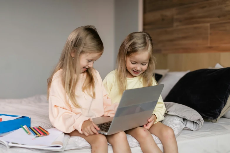 two little girls are on a bed with their laptops