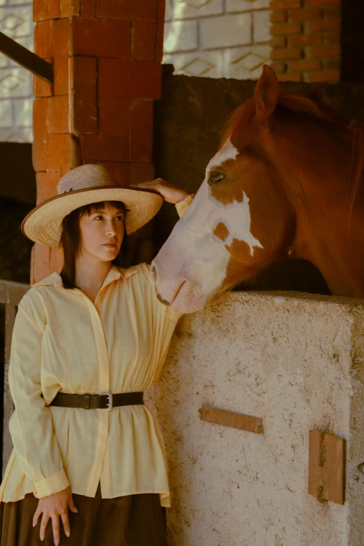 a woman in a hat leaning over a wall beside a horse