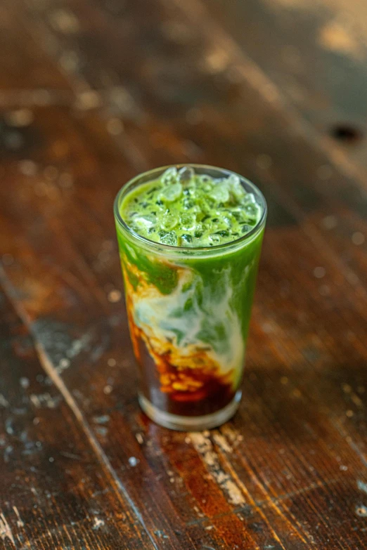 a glass with some green stuff inside on a wooden table