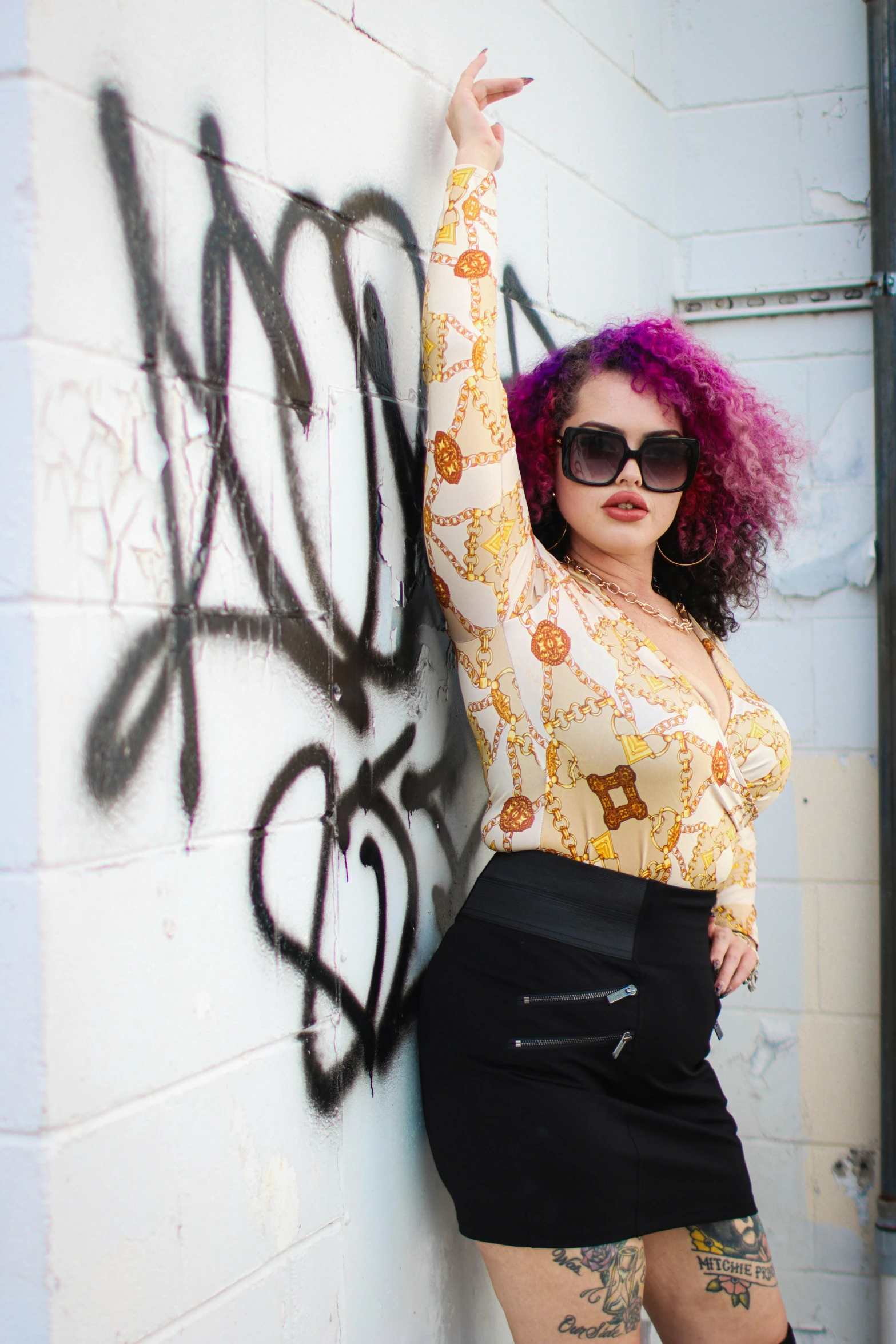 a woman with her hand in the air leaning against a wall covered in grafitti