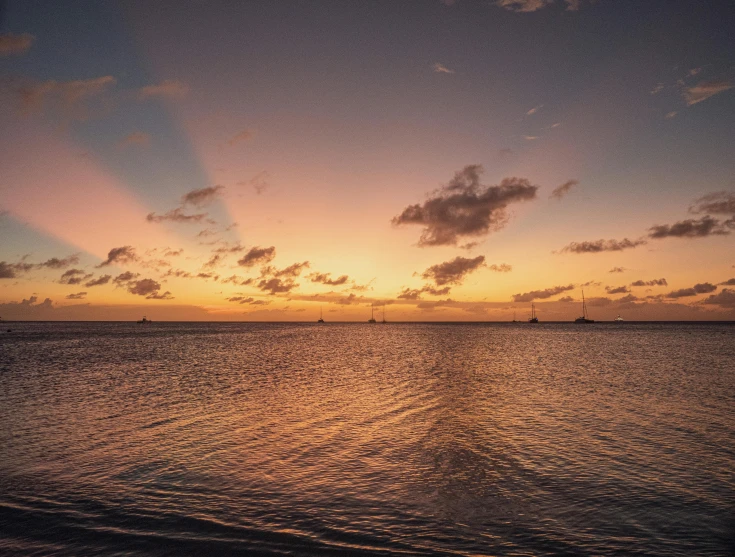 an ocean with boats in the distance at sunset