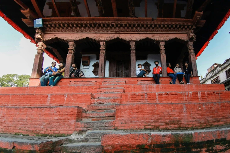 several people are sitting outside on a red brick wall