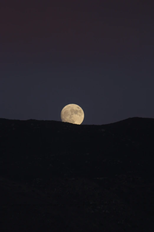 a night sky view with the moon setting behind a mountain