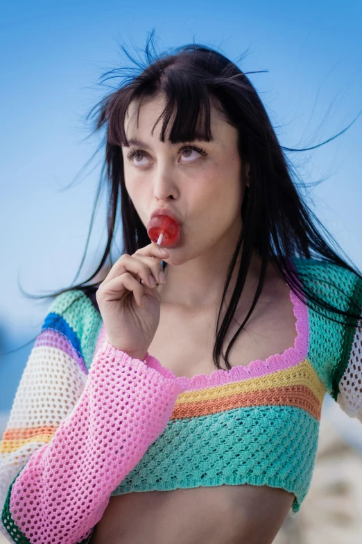 young woman in multicolored knit top making face, holding candy lollipop