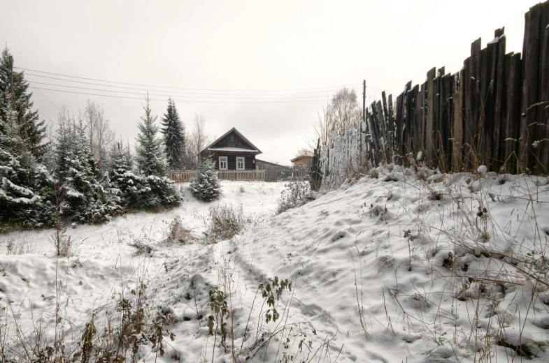 a dirt road covered with snow near a fence and houses