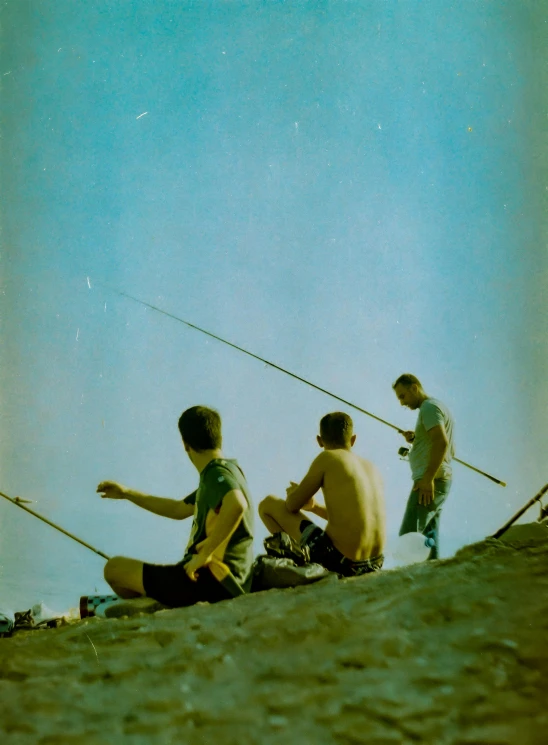 four young men sitting on the sand looking at soing