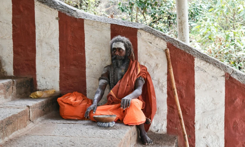 a man sitting outside of an old structure wearing a orange robe and head dress