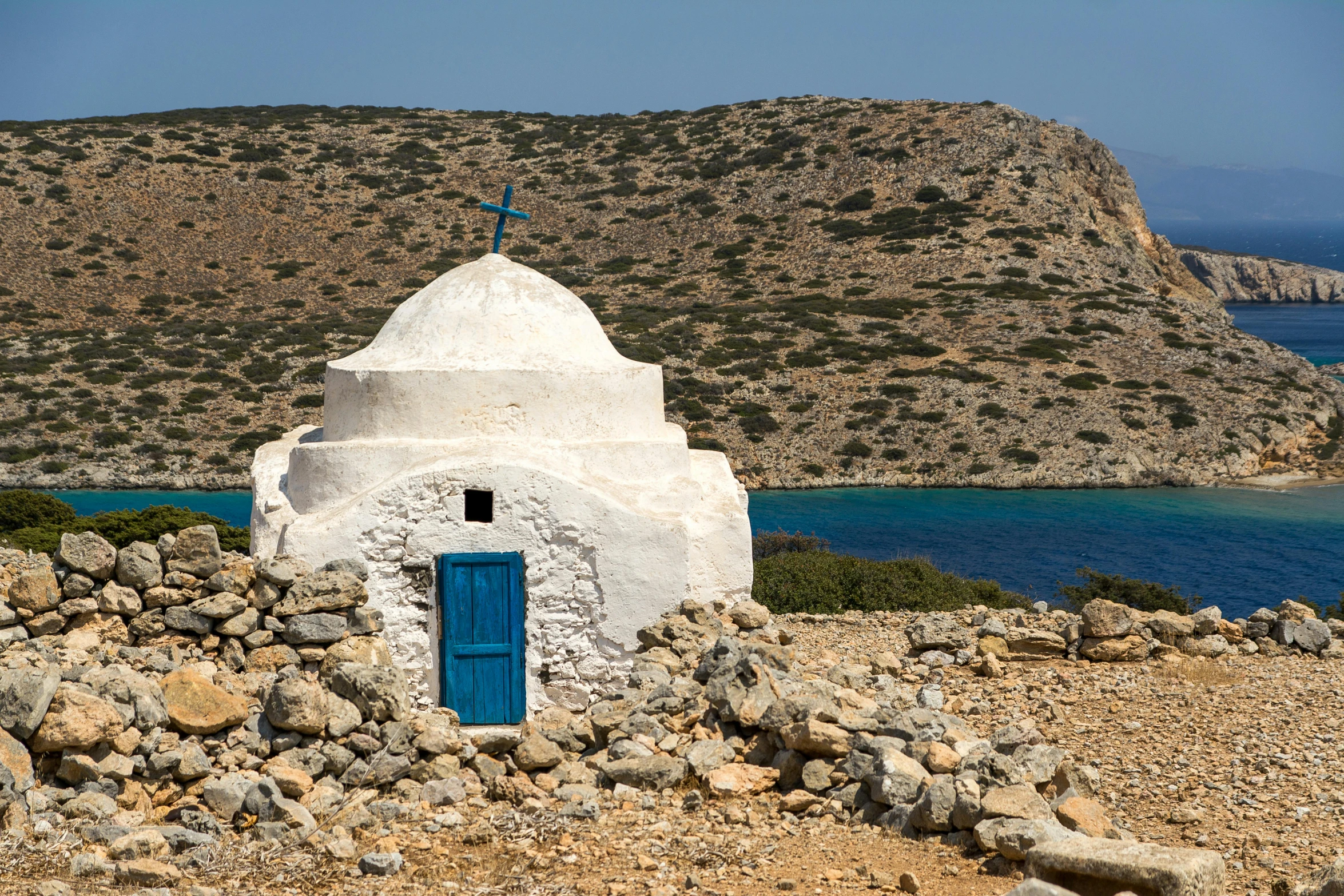 a small white structure with a blue door next to a mountain side