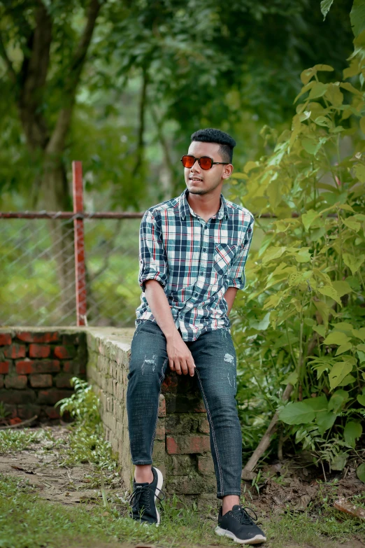 a man sitting on a wall near trees with sunglasses on