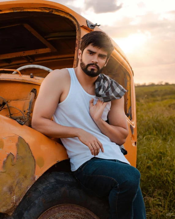 a man with a tie sits on the hood of an abandoned tractor