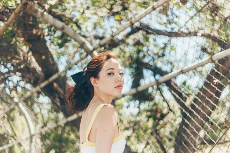 woman in white top leaning on fence with her back to the camera