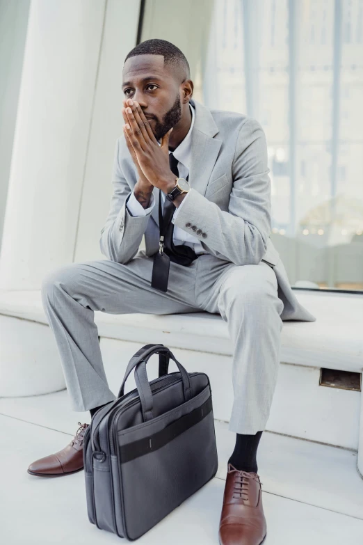 a man in a suit is sitting on a bench with his hands in his mouth