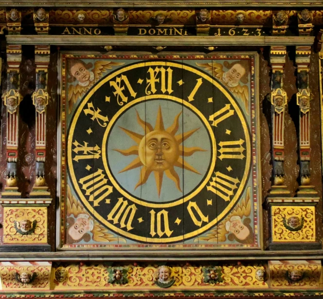 a clock with a sun on it is shown in an ornate decorated frame