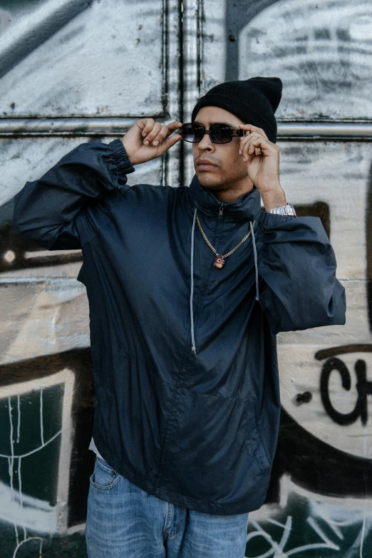 the man is wearing sunglasses and posing by a graffiti wall