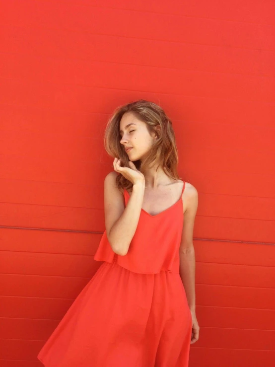 a woman wearing an orange dress is standing against a red wall