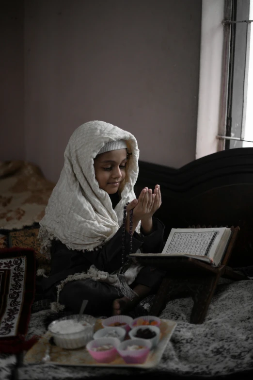 a young woman in a hijab prays before she is seated on the bed