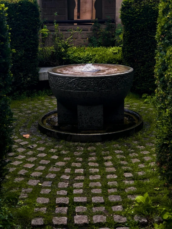 a courtyard area with a brick walkway, round stone fountain and trimmed hedges