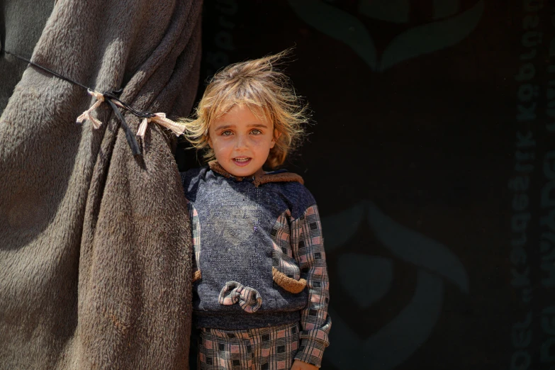 a child with blonde hair is holding onto a gray blanket