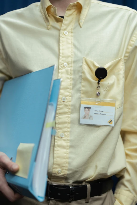 a man wearing a badge on his lap top is holding a folder and a binder