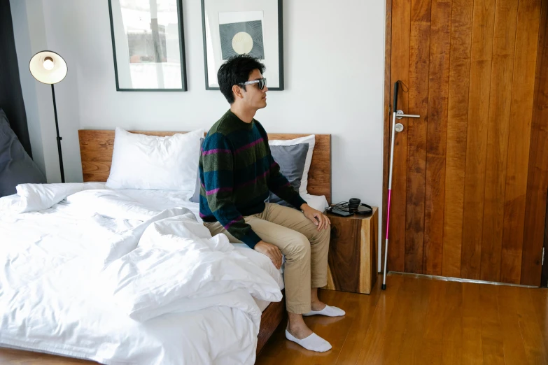 a man is sitting on his bed with white blankets