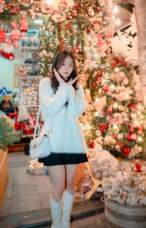 a woman in white boots poses with a christmas tree in the background