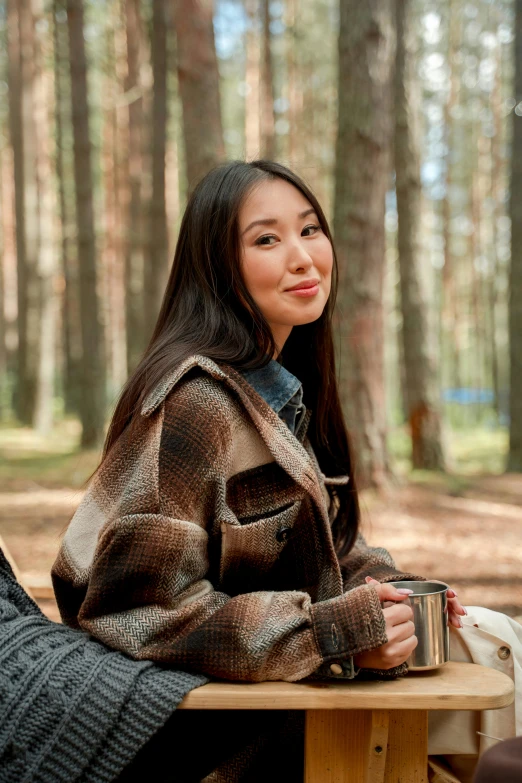 a woman in the woods is sitting on a bench with her mug