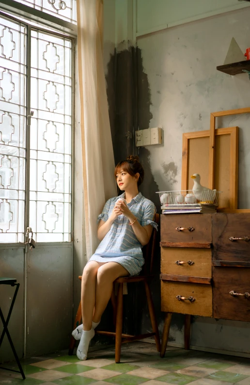 woman in blue dress seated in front of a window