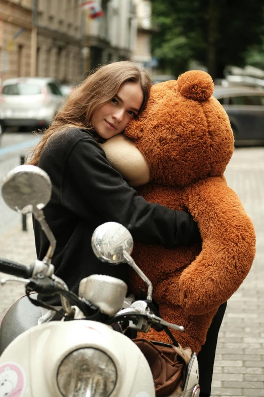 a beautiful woman hugging a large teddy bear on a motor scooter